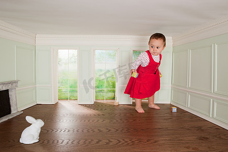 混乱家居摄影照片_一个蹒跚学步的女孩在一个小房间里看着兔子