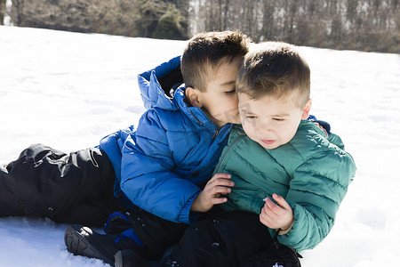 哥哥坐在雪地上对学龄前男孩窃窃私语