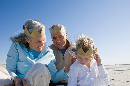 祖父母和孙女在海滩上戴着纸冠