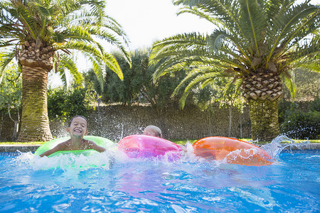 花园游泳池摄影照片_三个孩子在花园游泳池的充气环上嬉戏