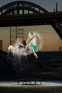 日落时分美国洛杉矶女芭蕾舞演员在蹦床上方跳跃同时释放粉末爆炸