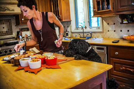 在宠物狗的注视下一名妇女在厨房柜台前准备零食