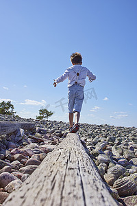 男孩在海滩上的原木上保持平衡