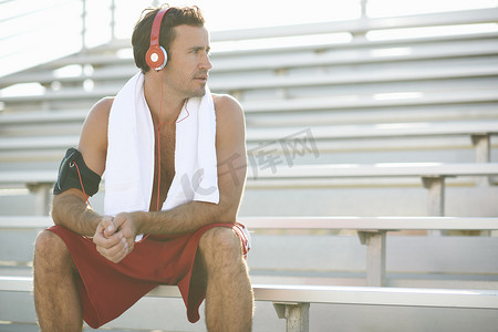 板凳摄影照片_中年男子坐在板凳上休息锻炼戴着耳机脖子上缠着毛巾