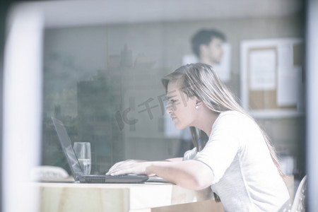 设计工作室中女设计师在笔记本电脑上工作的窗口视图