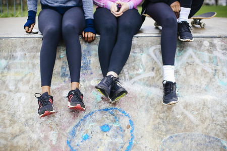 三名年轻女子滑板运动员坐在滑板公园的腰部以下的景色