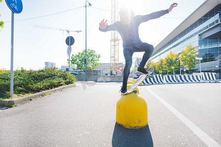 运动休闲裤子摄影照片_年轻的城市男子滑板运动员在黄色护栏上保持平衡