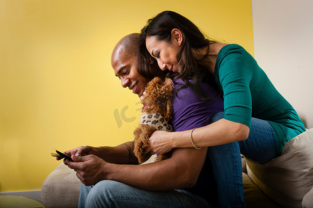 一对带着狗和智能手机坐在沙发上的中年夫妇