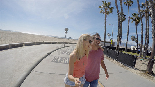 中年女性大笑摄影照片_美国加利福尼亚州威尼斯海滩一对滑冰时大笑的情侣自拍