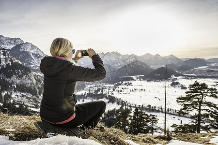智能造摄影照片_年轻女性徒步旅行者在智能手机上拍摄阿尔高阿尔卑斯山德国巴伐利亚州