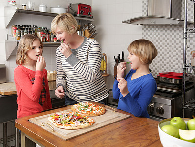 两个在柜台摄影照片_母亲和两个女儿在厨房里做饭一点点地吃着食材