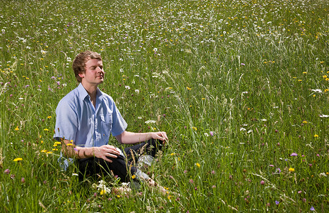 盘腿坐着摄影照片_一个男人坐在开着春花的草地上