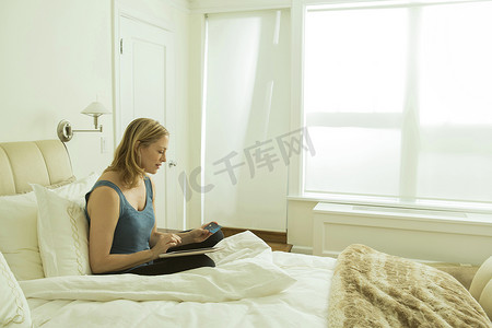 坐在床上的女性在数字平板电脑上阅读更新