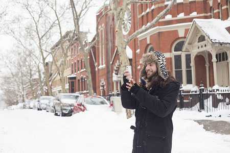 一名年轻人在白雪覆盖的街道上用智能手机阅读短信