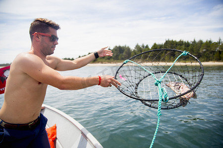 苹果游戏摄影照片_美国俄勒冈州尼哈勒姆湾一名中年男子从渔船上投掷诱饵捕蟹器