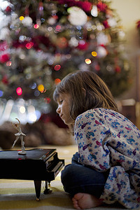 圣诞节坐在客厅地板上听玩具钢琴音乐盒的女孩
