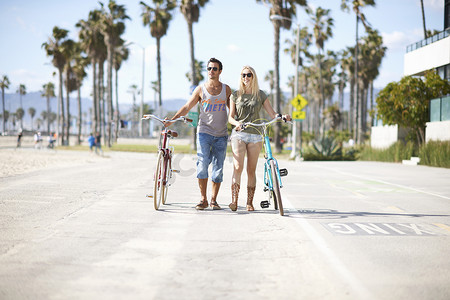骑情侣摄影照片_美国加利福尼亚州洛杉矶威尼斯海滩一对骑自行车的情侣骑着自行车散步