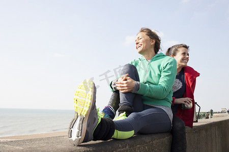 两名女跑步者在布赖顿海滩的墙上喝咖啡休息