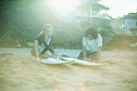 地板打蜡摄影照片_一对情侣坐在海滩上给冲浪板上蜡