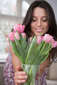 花瓶粉花摄影照片_一名中年妇女手持一瓶粉红色的花