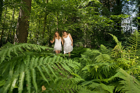 两个十几岁的女孩手牵着手穿过森林