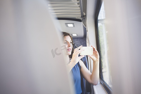 火车上的中年妇女用智能手机透过车窗拍照