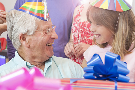 派对装饰摄影照片_祖父和孙女戴着派对帽面对面微笑