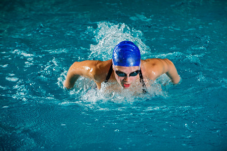 健身游泳池摄影照片_十几岁的女孩戴着泳帽和护目镜在游泳池里游泳