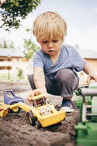 蹲在泥里看着玩耍玩具卡车的男孩