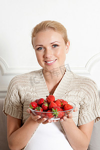 微笑的女人端着一碗草莓
