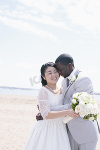 海滩上的新娘和新郎手持新娘花束拥抱微笑着