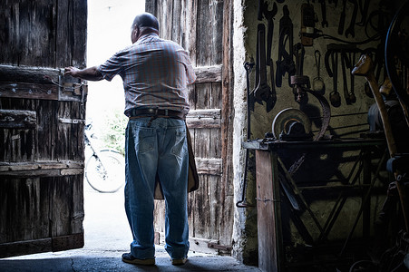 意大利撒丁岛卡利亚里高级男性铁匠在打开传统谷仓的门时的背影