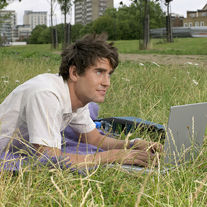 斜躺着摄影照片_公园里躺着一位拿着笔记本电脑的年轻人