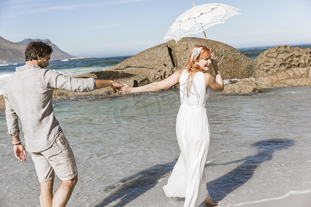 情侣手牵手走在海岸线上撑着伞望着肩微笑着