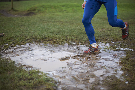 跑步者的腿在泥泞的水坑中奔跑