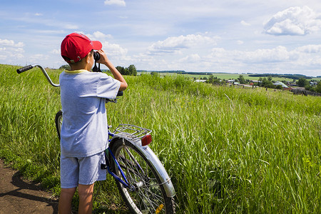 投用摄影照片_小男孩骑着自行车站在田野边用双筒望远镜看风景后视镜