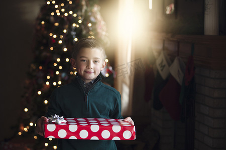 点波摄影照片_圣诞树前拿着礼物的男孩微笑着看着相机