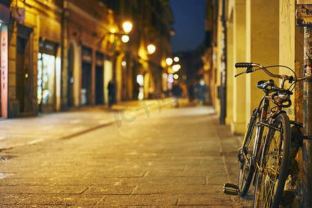意大利街摄影照片_夜间意大利博洛尼亚自行车靠在街壁上
