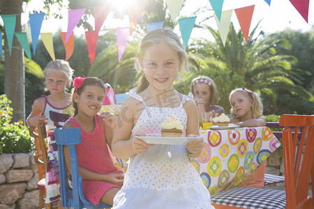 9岁生日摄影照片_生日聚会上的女孩拿着带纸杯蛋糕的盘子
