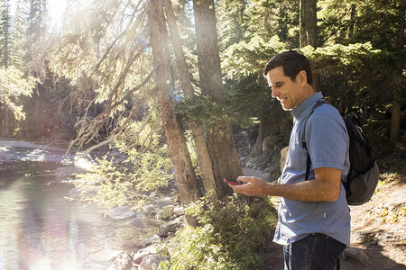加拿大阿尔伯塔省坎莫尔森林河岸一名资深男性徒步旅行者在看智能手机