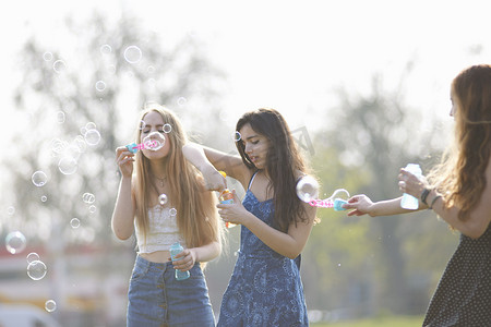 三个十几岁的女孩在公园里用泡泡棒吹泡泡