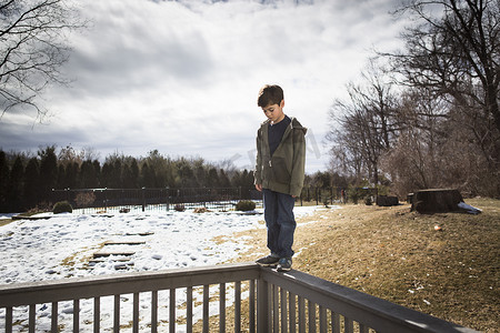 冬栅栏摄影照片_公园里的男孩在栅栏顶上保持平衡