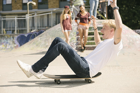 在城市滑板公园里年轻的男子滑板运动员坐在滑板上移动