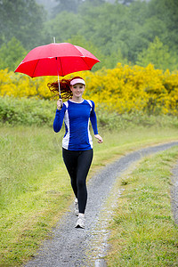 少女撑着雨伞摄影照片_美国华盛顿州班布里奇岛十几岁的女孩撑着伞在土路上奔跑