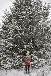 雪摄影照片_年轻的女孩站在一棵大的常绿树前被雪覆盖着