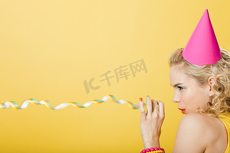 彩色飘带装饰摄影照片_戴着派对帽和派对飘带的年轻女子