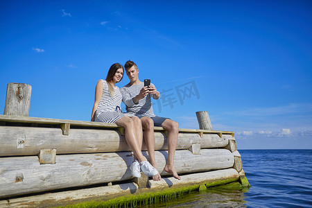 一对情侣坐在木质码头上用智能手机自拍