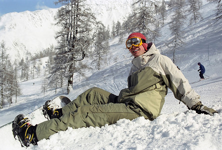 拿着滑雪板坐在雪地里的男孩