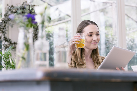 一杯橙汁摄影照片_一名年轻女子手持一杯橙汁使用数字平板电脑