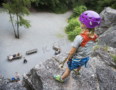 戴着攀岩头盔的男孩站在岩石顶上往下看